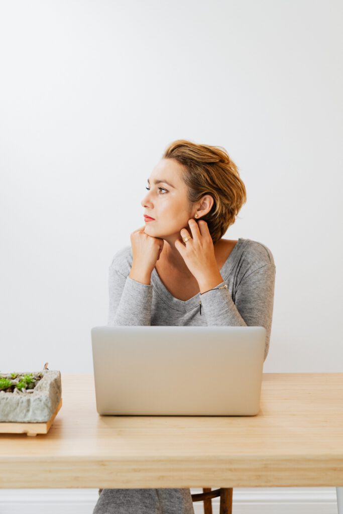 Woman sitting behind a laptop and looking away while feeling mentally stuck