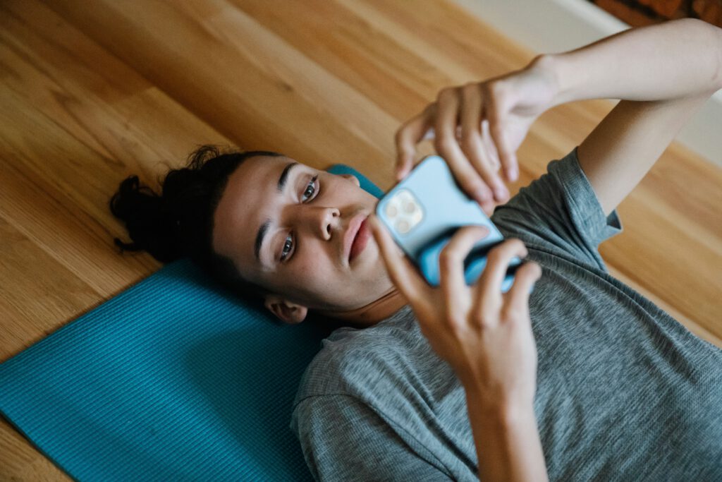 Person lying on an exercise mat and scrolling on a phone instead of beginning