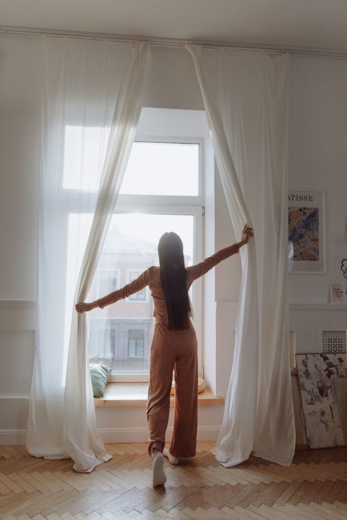 Woman opening bedroom curtains to morning daylight